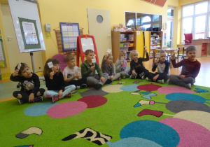 Grupa dzieci siedzi skrzyżnie z uniesionymi tabliczkami z napisem nie, ocenia w ten sposób słuszność zdania wypowiedzianego przez nauczyciela.